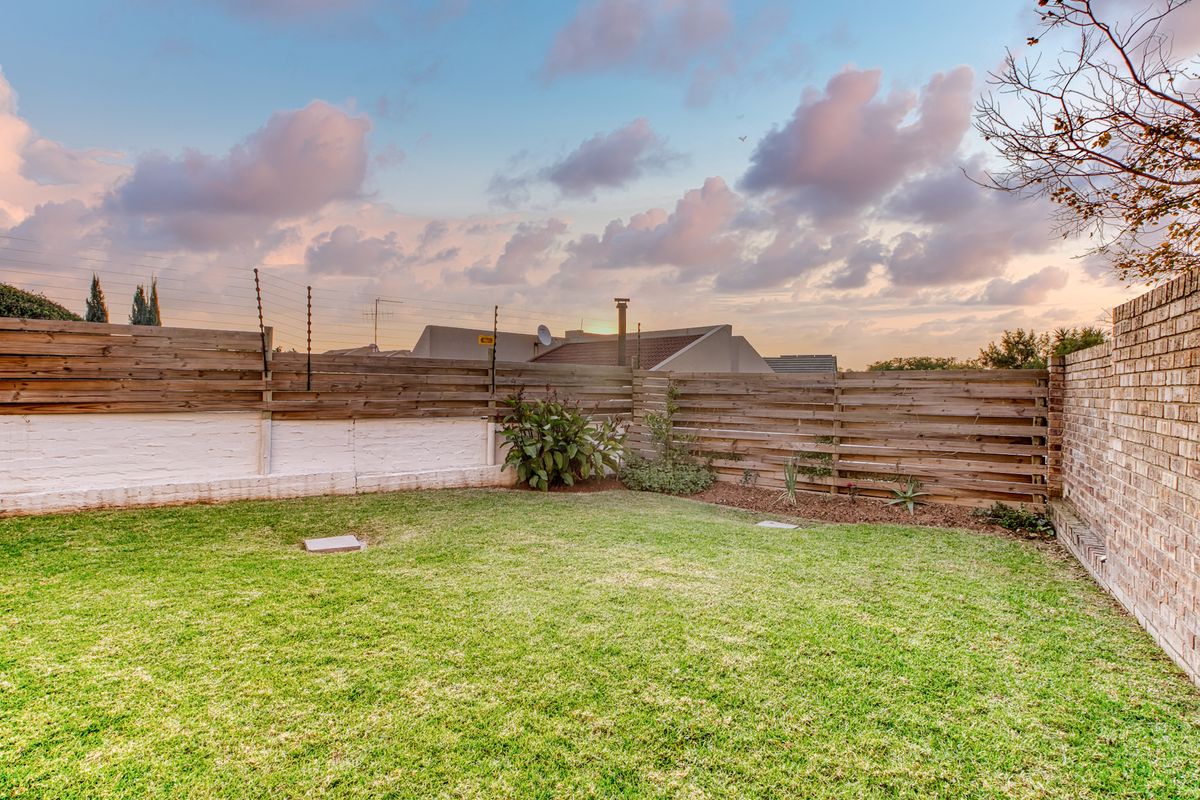 A private rear garden featuring a well-maintained lawn, enclosed by a combination of timber slat fencing and a brick boundary wall with electric security.