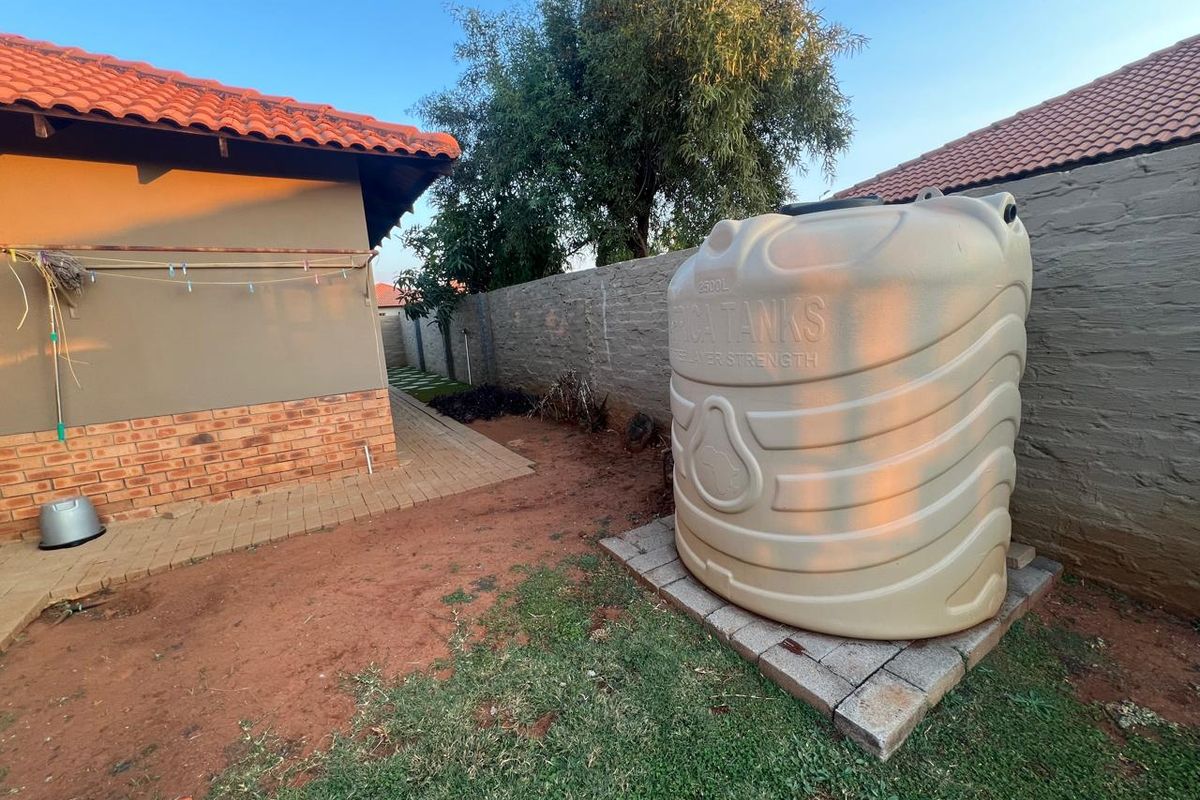 Rear exterior area featuring a large water storage tank, paved walkway, and brick boundary wall.