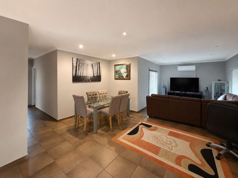 Spacious open-plan living and dining area featuring neutral wall tones, tiled flooring, recessed lighting, and a wall-mounted air conditioning unit.