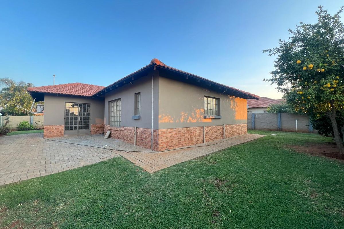 Rear view of the house featuring a paved patio area, brick and plaster exterior walls, tiled roof, and a well-maintained garden.