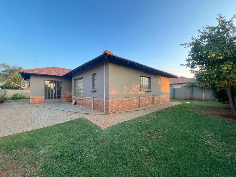 Rear view of the house featuring a paved patio area, brick and plaster exterior walls, tiled roof, and a well-maintained garden.