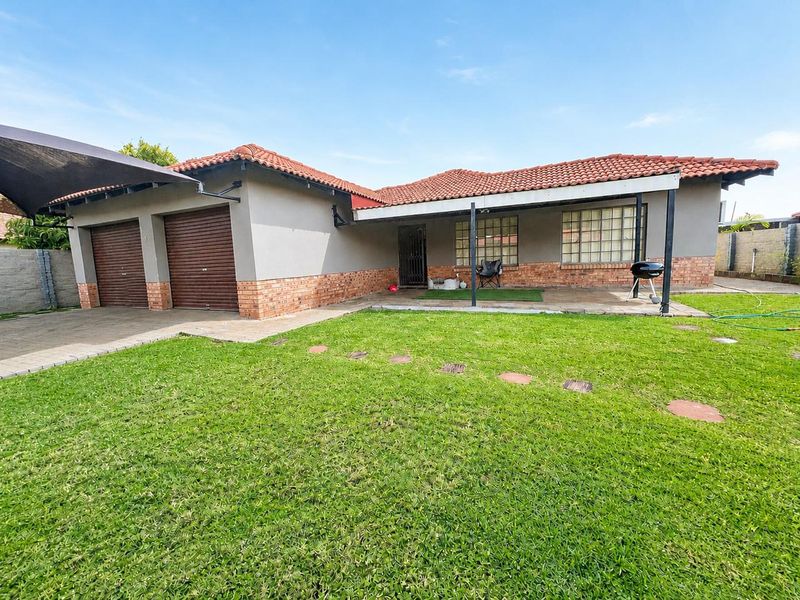 Rear view of the property featuring a double garage, covered patio area, and a well-maintained lawn.