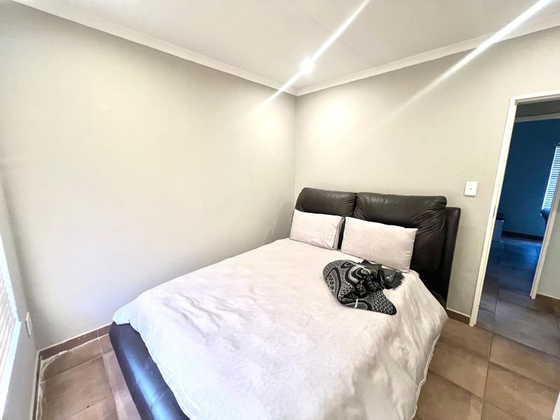 A compact bedroom featuring tiled flooring and neutral wall finishes, providing a functional space with direct access to an adjoining room.