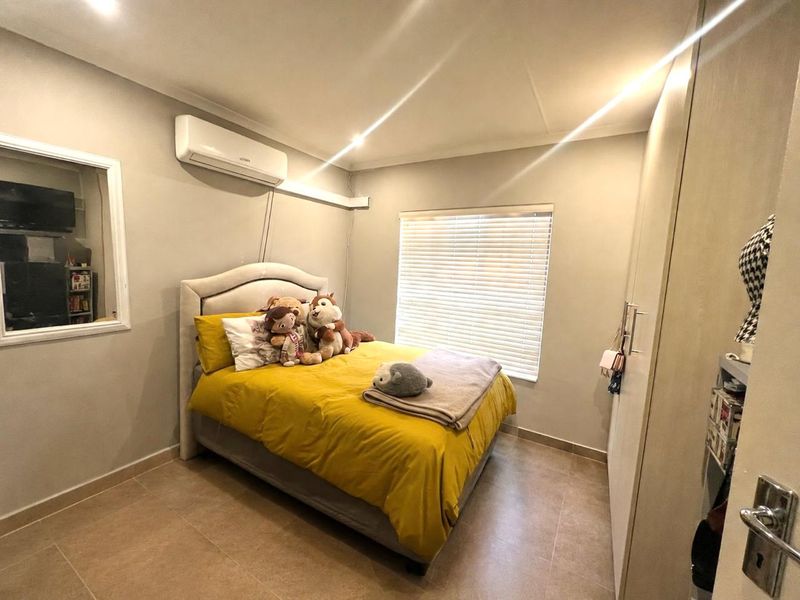 A well-maintained bedroom featuring tiled flooring, a built-in wardrobe, venetian blinds, and a wall-mounted split-system air conditioning unit.