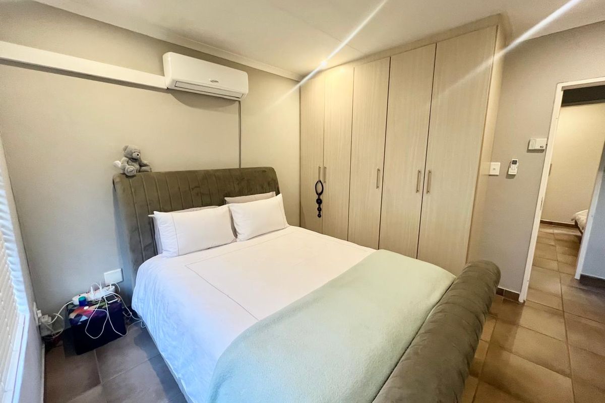 A well-maintained bedroom featuring built-in wooden cupboards, tiled flooring, and a wall-mounted split-system air conditioning unit.