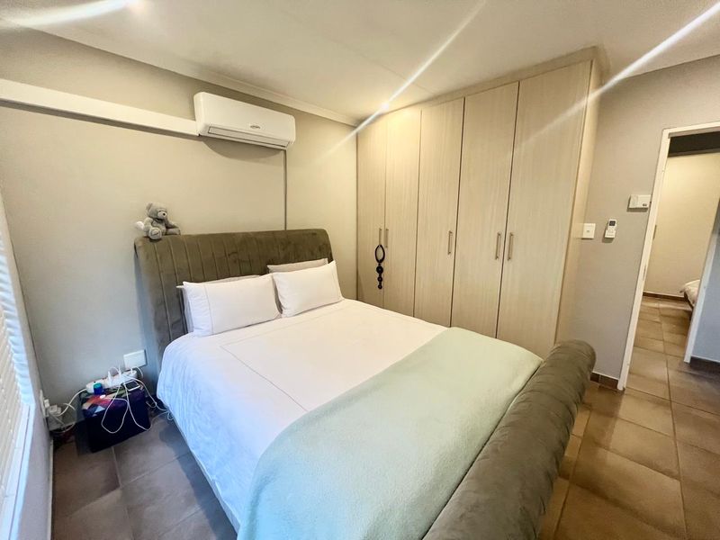 A well-maintained bedroom featuring built-in wooden cupboards, tiled flooring, and a wall-mounted split-system air conditioning unit.