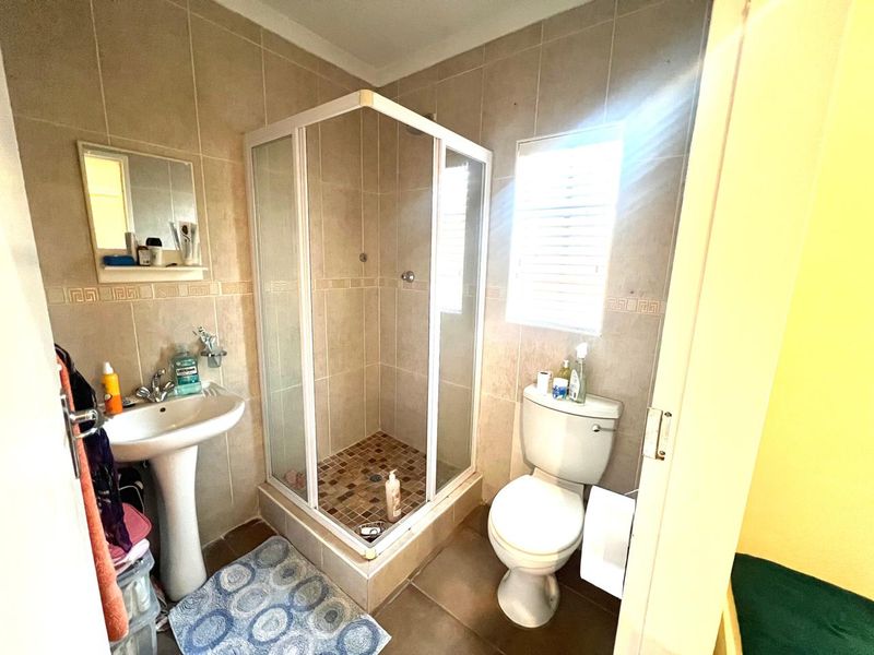A functional bathroom featuring a pedestal basin, a corner shower enclosure, and a standard toilet with neutral wall and floor tiling.