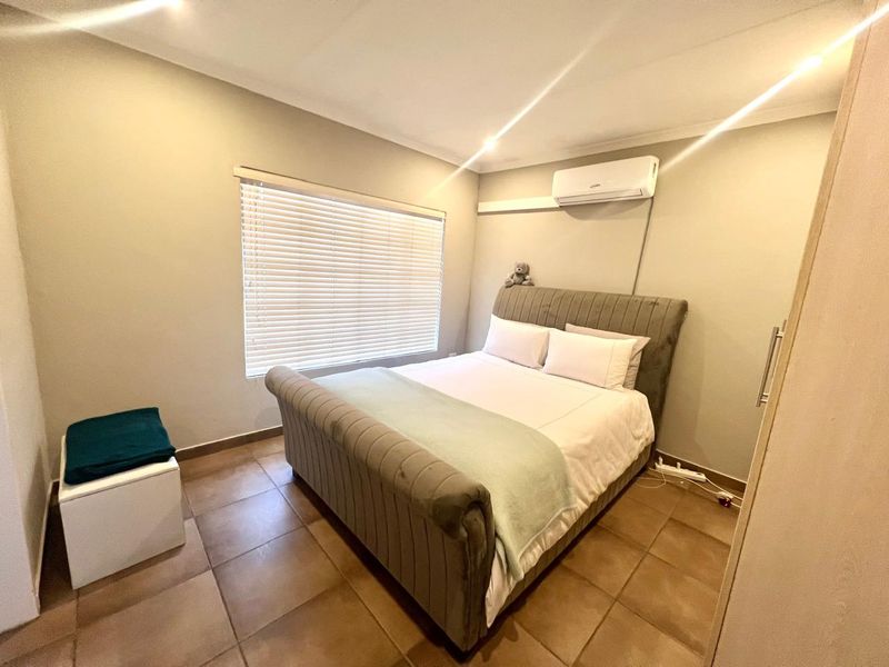 A well-maintained bedroom featuring tiled flooring, an integrated air conditioning unit, and venetian blinds for privacy.
