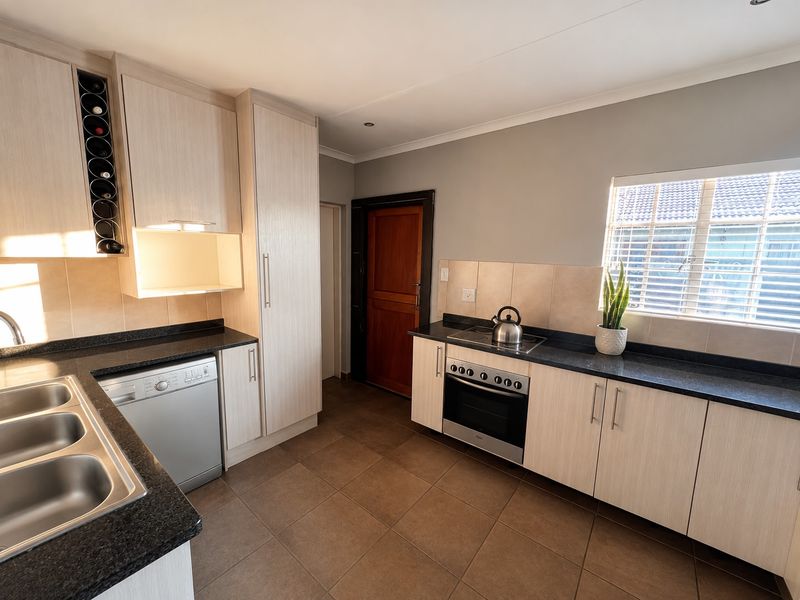 Modern kitchen featuring light wood cabinetry, granite countertops, integrated dishwasher, built-in oven, and hob with tiled flooring and ample storage space.