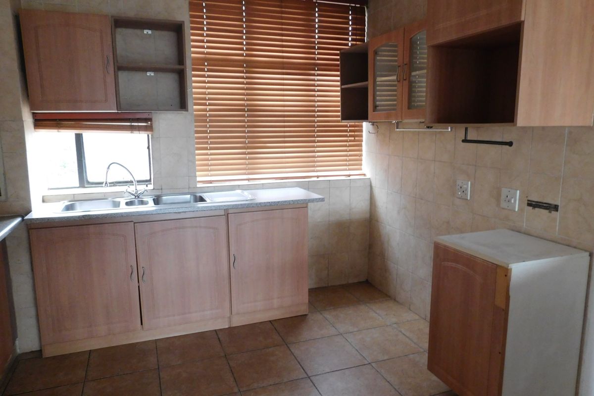 A functional kitchen featuring laminate cabinetry, double bowl sink, and tiled finishes. The space is currently vacant and requires cosmetic updates to modernize.