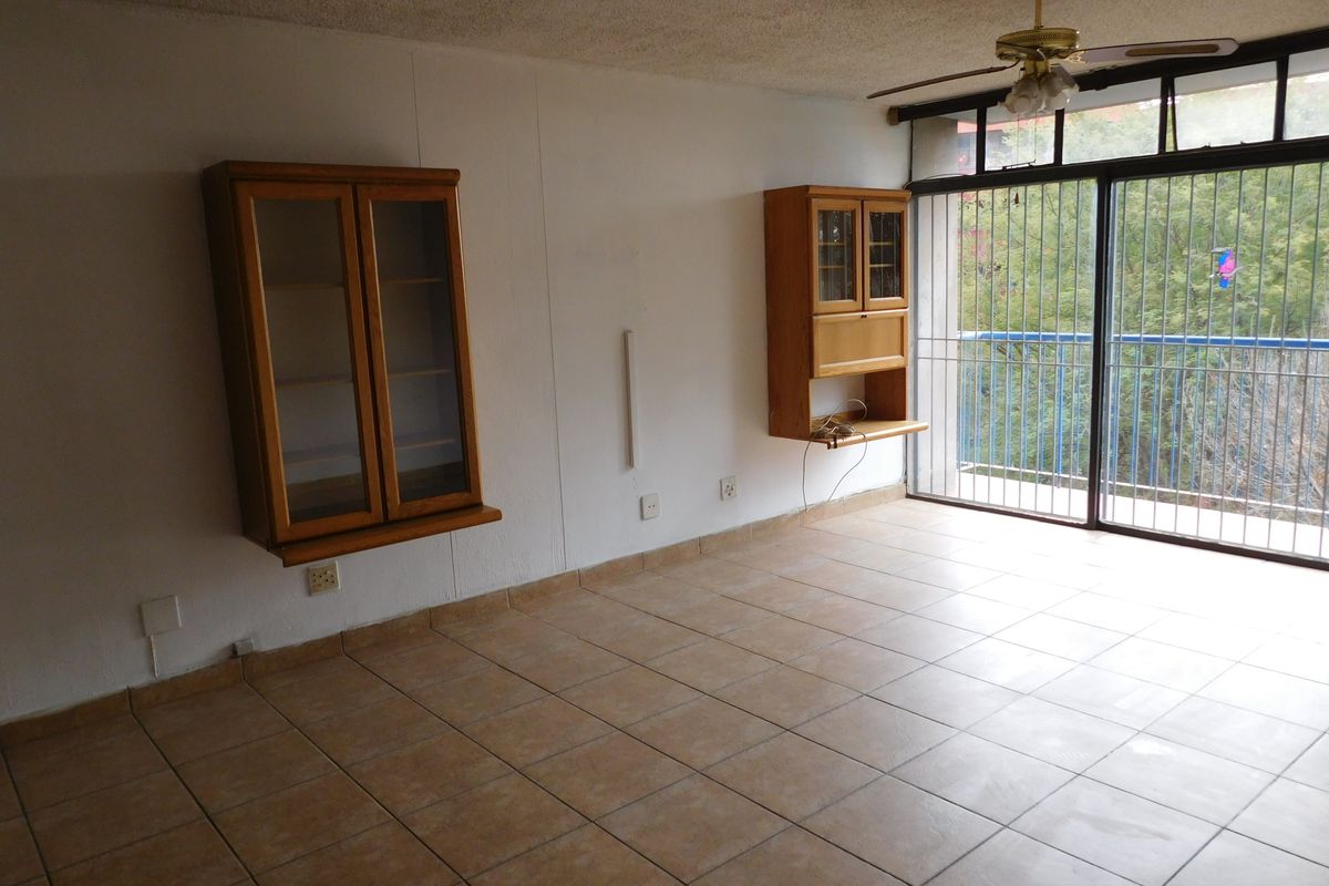 An empty living room featuring tiled flooring, a ceiling fan, and wall-mounted cabinetry, with access to a balcony through a sliding glass door.