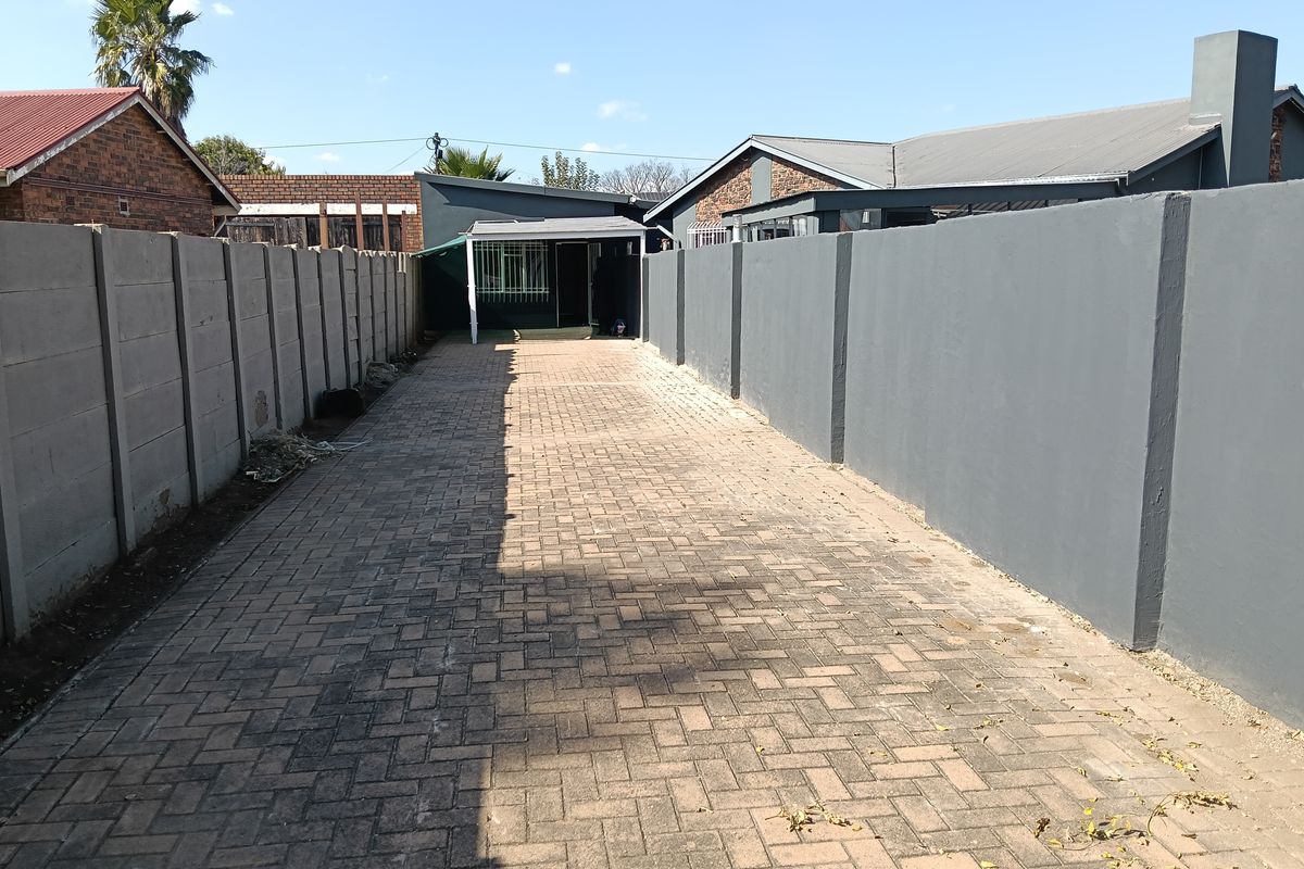 A long paved driveway leading to a covered patio area, enclosed by high perimeter walls.