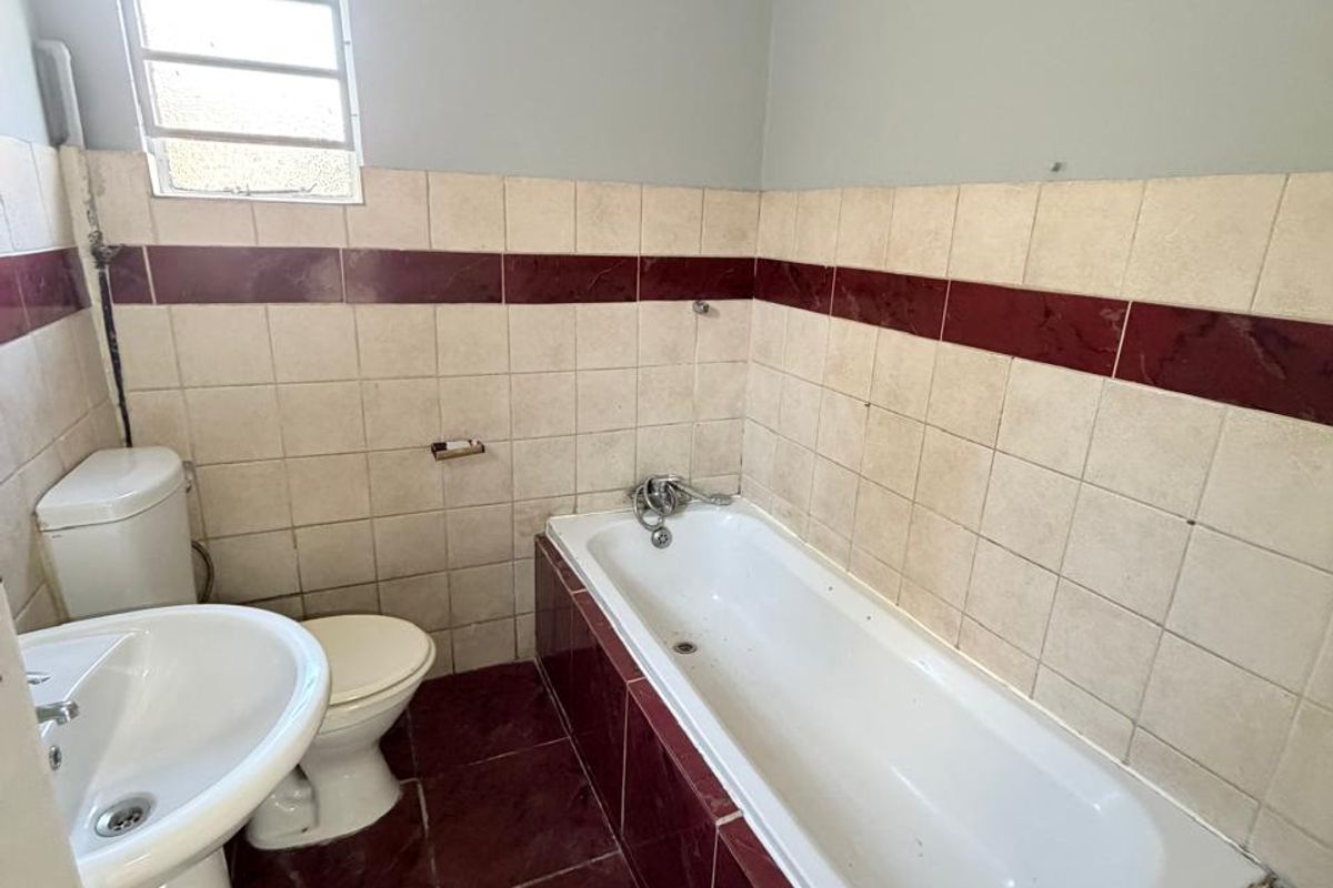 A functional bathroom featuring a pedestal basin, toilet, and built-in bathtub with tiled surround, requiring cosmetic updates to modernize the space.