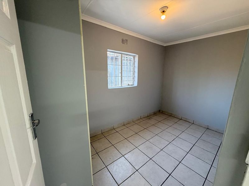 A clean, empty bedroom featuring neutral grey walls, tiled flooring, and a window fitted with security bars.