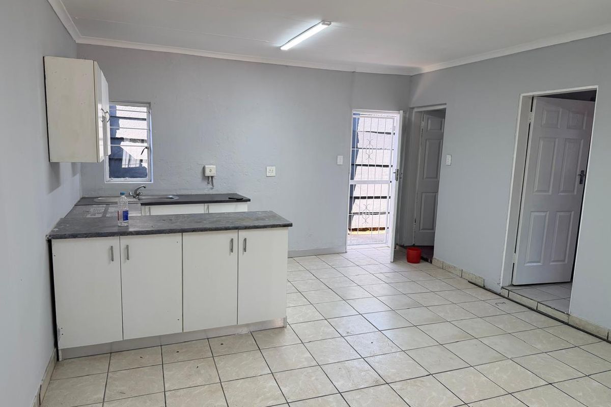 A functional, empty kitchen area featuring basic cabinetry, laminate countertops, and tiled flooring, providing a blank canvas for potential updates.