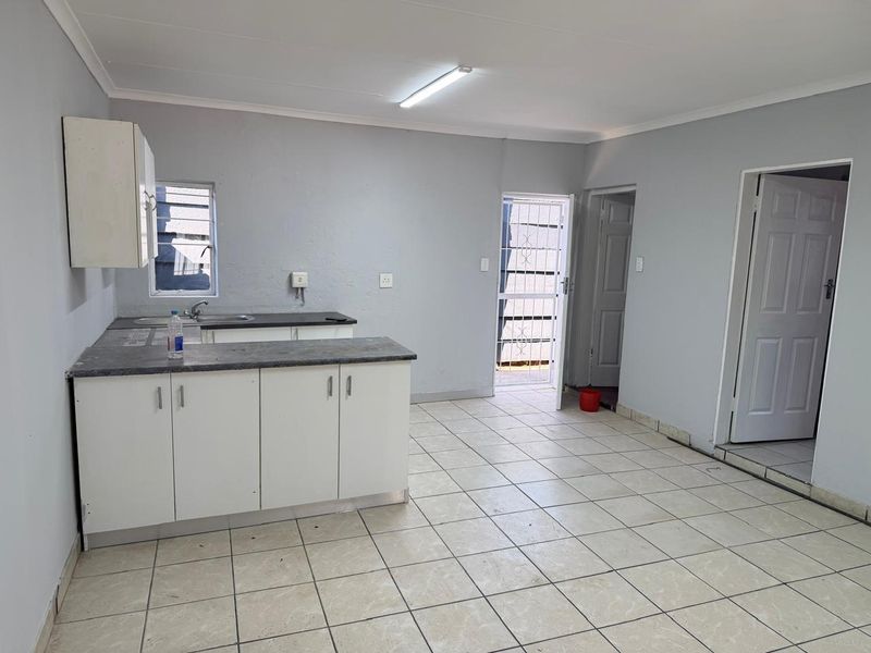 A functional, empty kitchen area featuring basic cabinetry, laminate countertops, and tiled flooring, providing a blank canvas for potential updates.