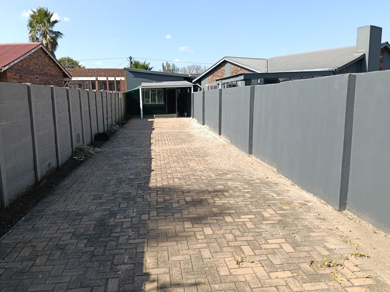 A long paved driveway leading to a covered patio area, enclosed by high perimeter walls.