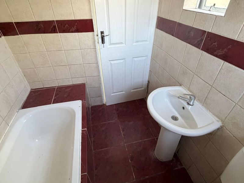 A compact bathroom featuring a pedestal basin, built-in bathtub, and toilet, finished with dated ceramic wall and floor tiles.