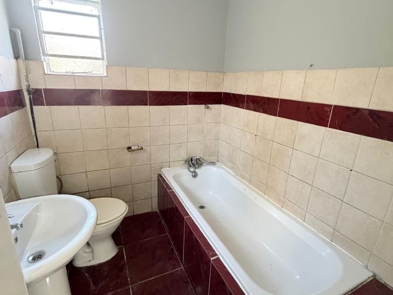 A functional bathroom featuring a pedestal basin, toilet, and built-in bathtub with tiled surround, requiring cosmetic updates to modernize the space.