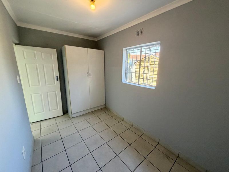 A compact bedroom featuring tiled flooring, a built-in wardrobe, and a window fitted with security bars.