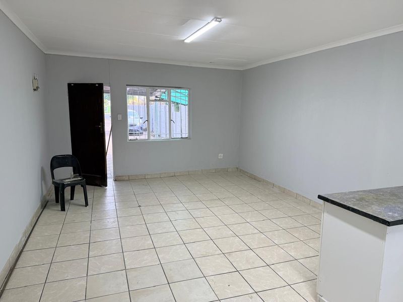 An open-plan living area featuring neutral tiled flooring, clean grey walls, and a functional kitchen counter, offering a versatile space for living and dining.