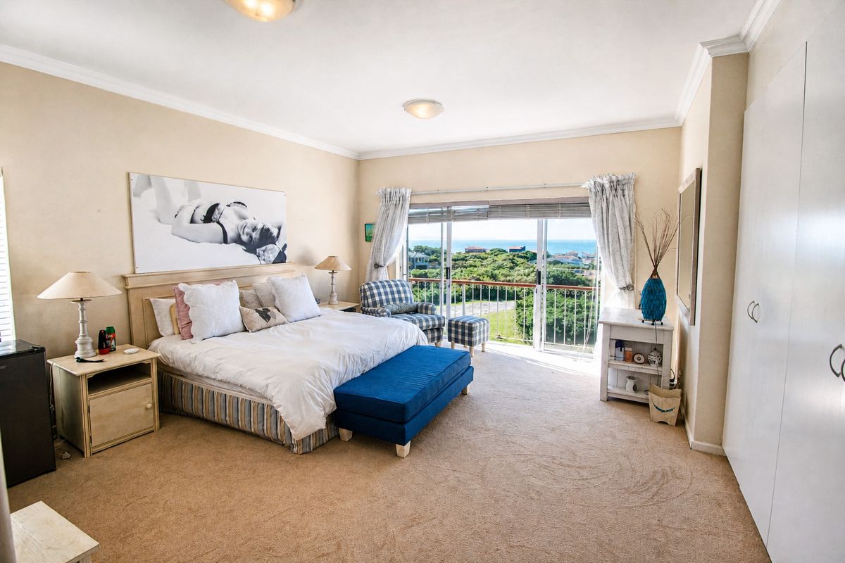 Spacious bedroom featuring neutral carpeting, built-in wardrobes, and sliding glass doors that open to a balcony with scenic coastal views.