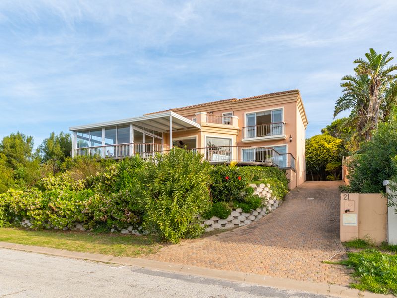 Front elevation of a multi-story residence featuring a paved driveway, landscaped garden, enclosed patio, and upper-level balcony with glass railings.