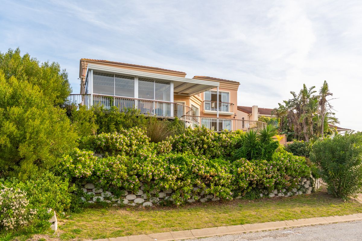 Rear elevation of a multi-level house featuring an enclosed balcony, metal railings, and a stone retaining wall set within a landscaped garden.