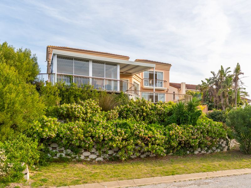 Rear elevation of a multi-level house featuring an enclosed balcony, metal railings, and a stone retaining wall set within a landscaped garden.