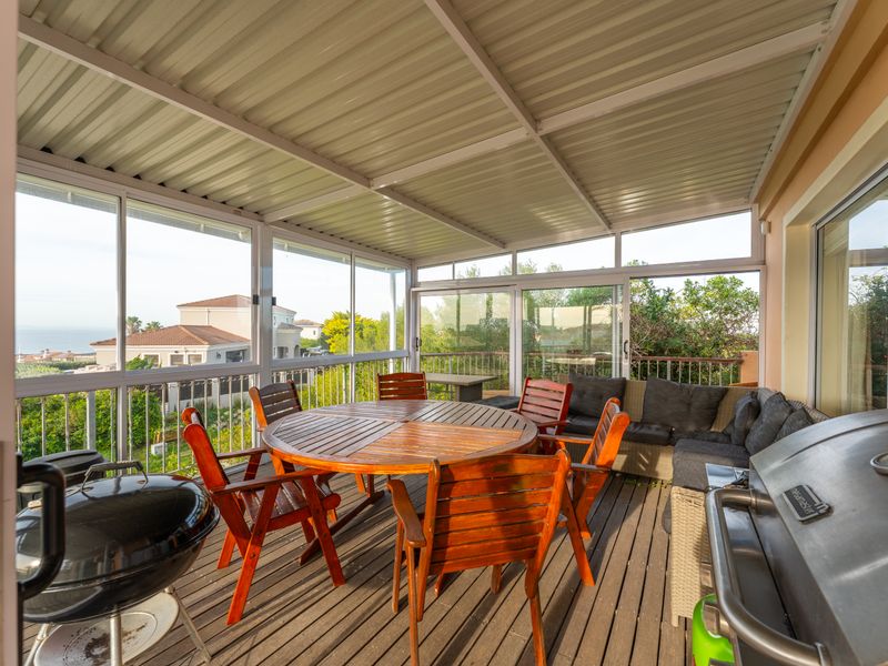 Enclosed patio featuring timber decking, a corrugated metal roof, and large sliding windows offering views of the surrounding neighborhood.