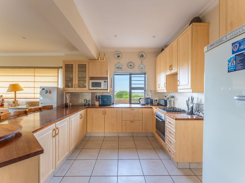 Open-plan kitchen featuring light wood cabinetry, timber countertops, built-in oven, gas hob, and tiled flooring, seamlessly flowing into the adjacent living area.