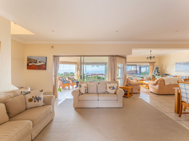 Spacious open-plan living and dining area featuring tiled floors, recessed lighting, and large sliding glass doors leading to an outdoor patio with coastal views.