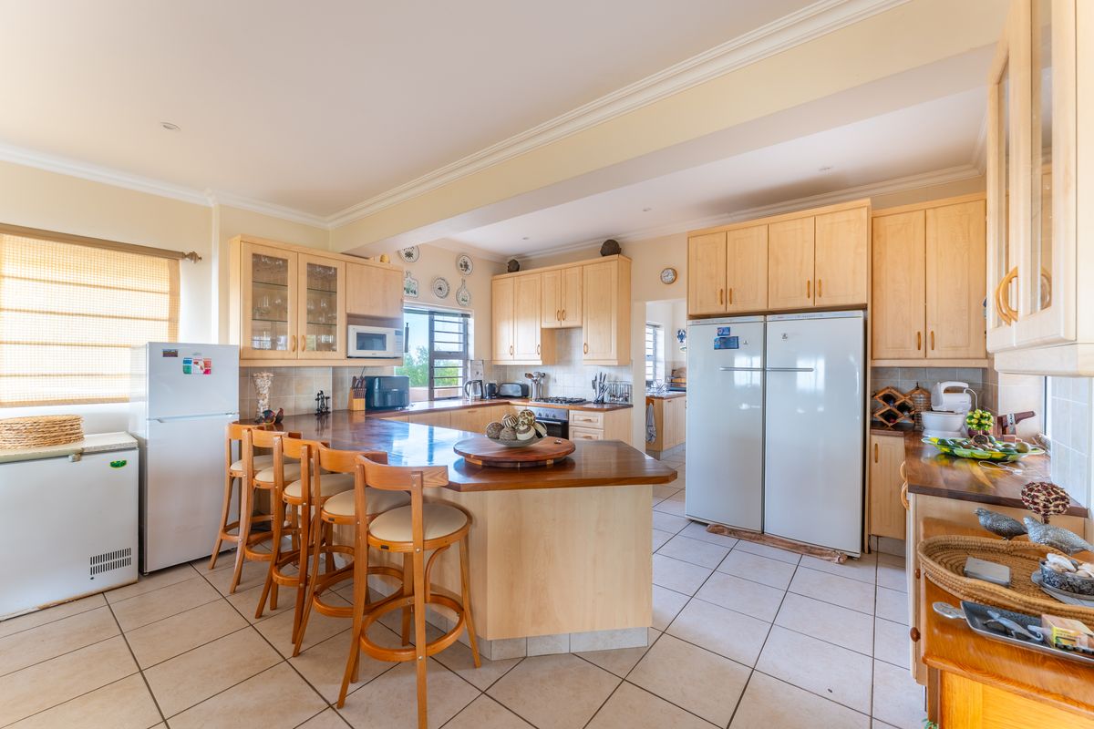 Spacious kitchen featuring light-wood cabinetry, a central breakfast bar, tiled flooring, and integrated appliances, offering a functional layout with ample storage space.