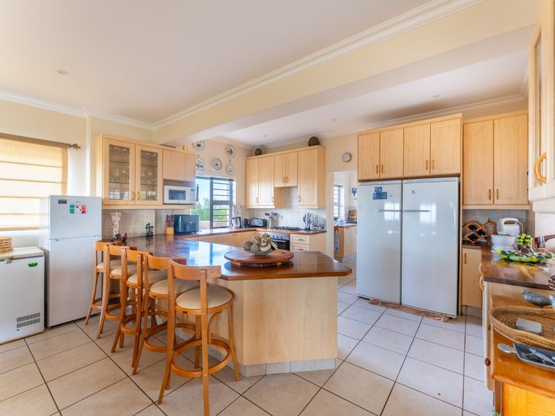 Spacious kitchen featuring light-wood cabinetry, a central breakfast bar, tiled flooring, and integrated appliances, offering a functional layout with ample storage space.