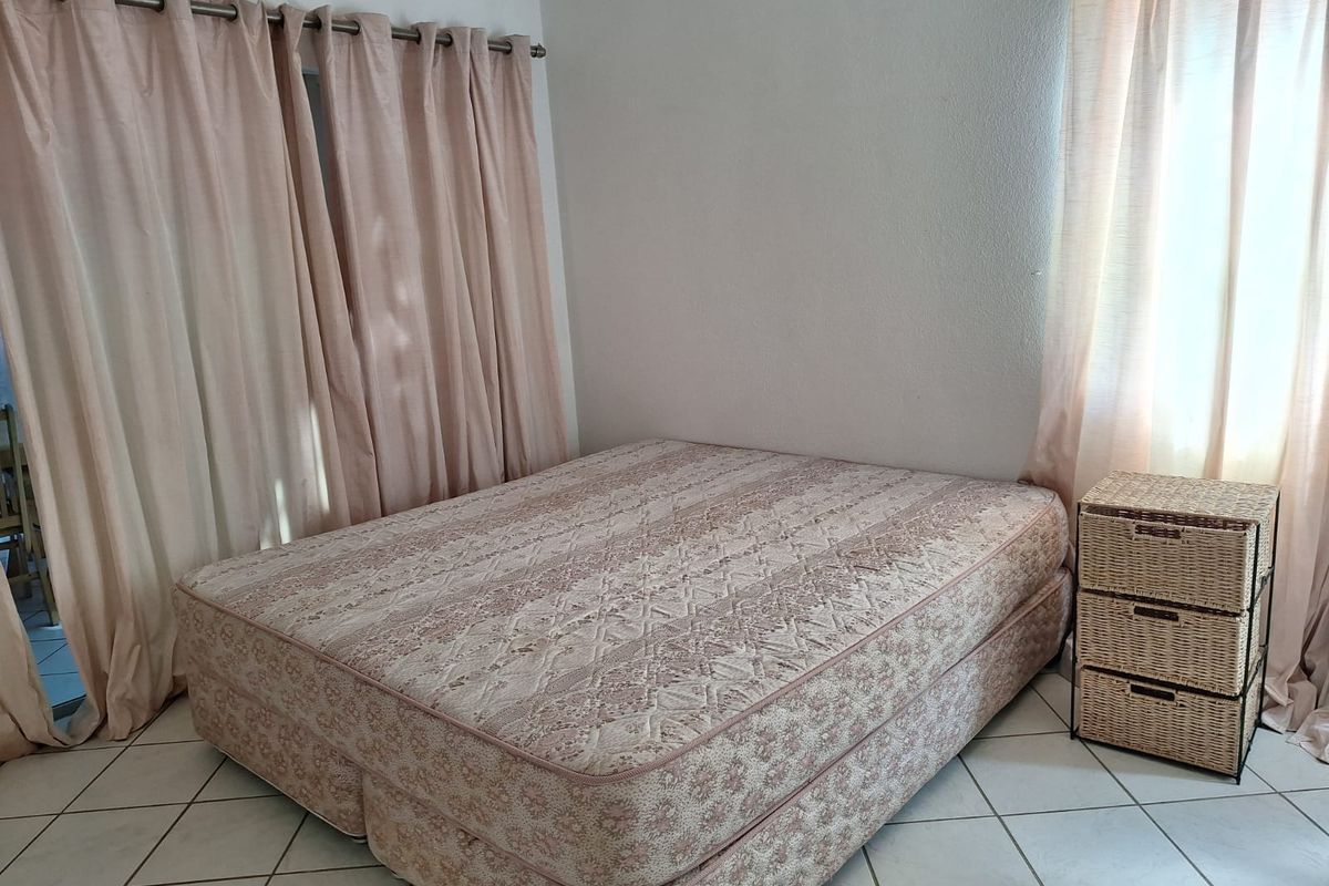 A bedroom featuring tiled flooring and a ceiling fan, with large windows dressed in curtains.