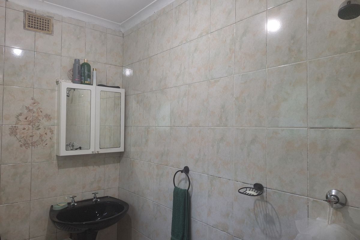 A dated bathroom featuring full-height wall tiling, a pedestal basin, and a wall-mounted medicine cabinet with integrated shower fixtures.