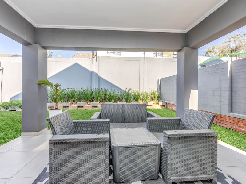 A well-maintained covered patio area featuring tiled flooring, overlooking a private garden enclosed by a secure perimeter wall.