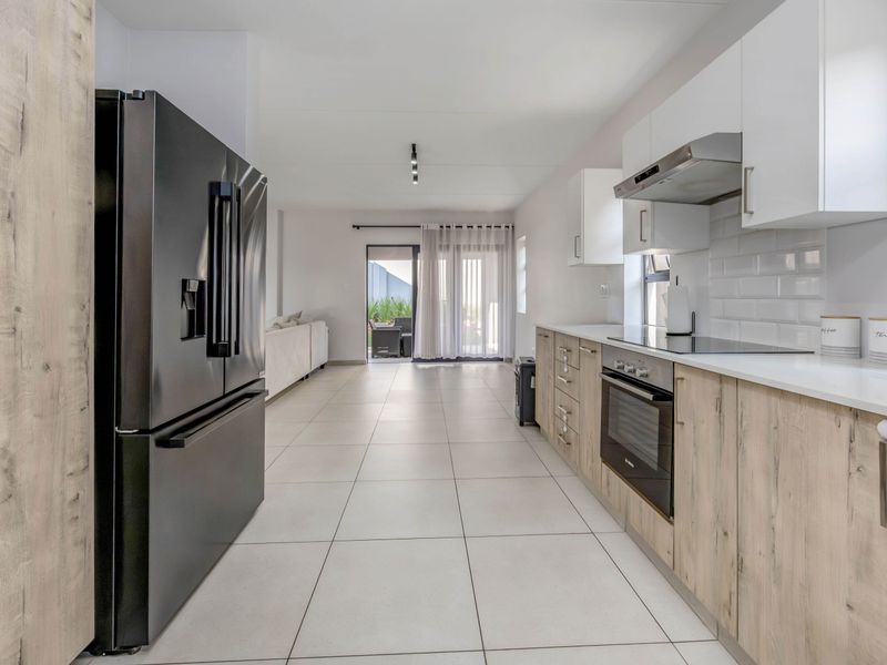 Modern open-plan kitchen featuring light wood-grain cabinetry, white countertops, subway tile backsplash, and integrated appliances, flowing into the living area with patio access.