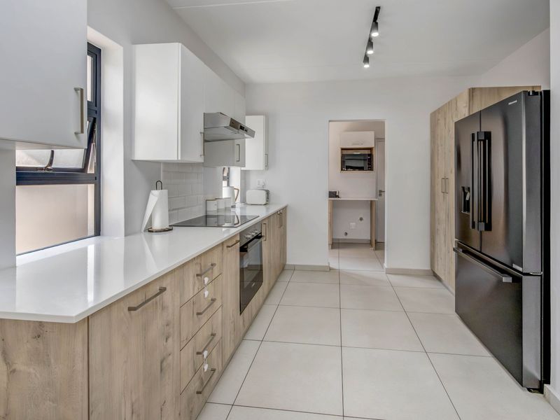 Modern kitchen featuring light wood-grain cabinetry, white quartz countertops, subway tile backsplash, and integrated appliances with a clean, contemporary aesthetic.