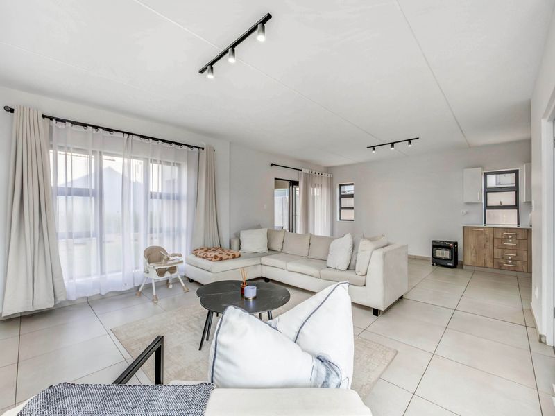 Spacious open-plan living area featuring neutral tiled flooring, modern track lighting, and large windows that provide ample natural light throughout the space.