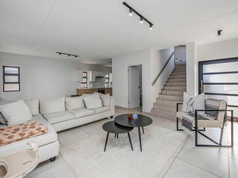 Modern open-plan living area featuring tiled floors, contemporary track lighting, and a staircase leading to the upper level, adjacent to a functional kitchen space.