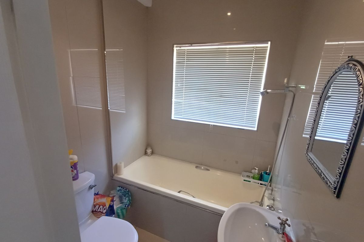 A functional bathroom featuring a bathtub with shower attachment, pedestal basin, toilet, and neutral wall tiling with a window for natural light.