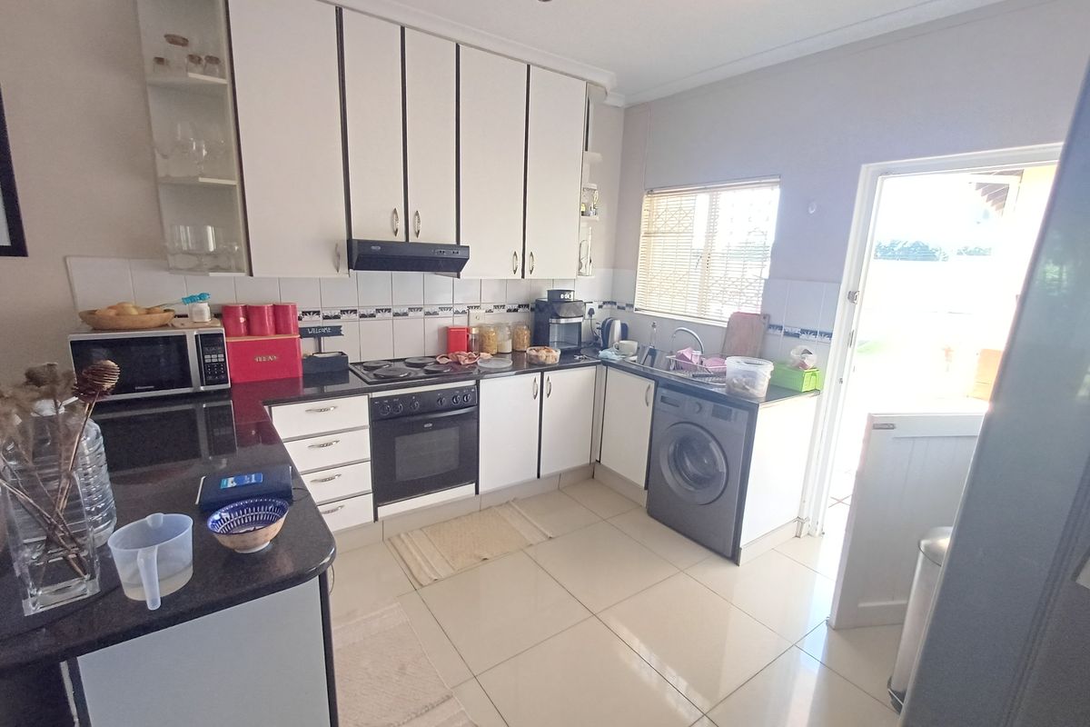 A functional kitchen featuring white cabinetry, dark countertops, tiled flooring, and an integrated washing machine with direct access to the exterior.