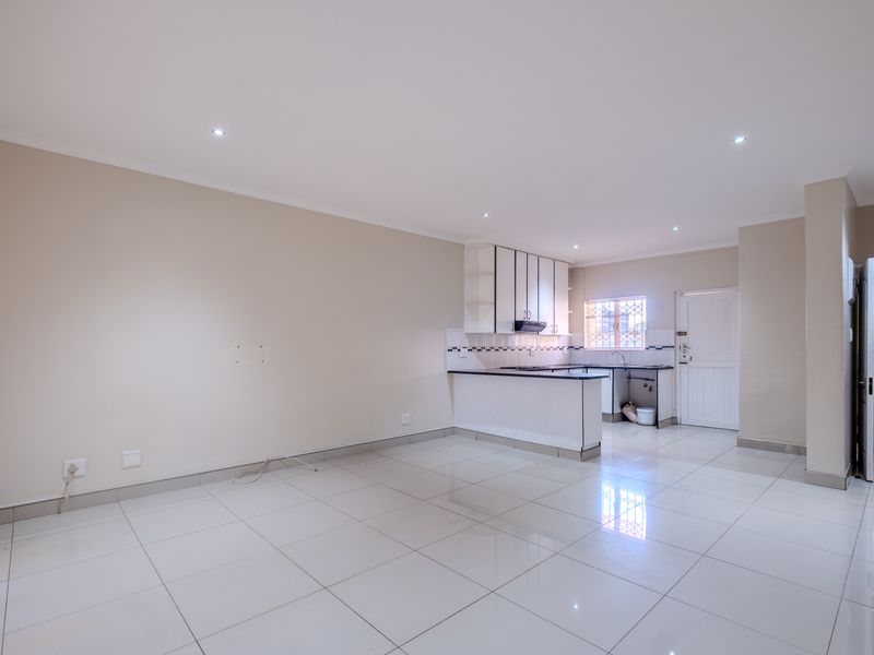 Spacious open-plan living area featuring tiled flooring, recessed lighting, and a functional kitchen with built-in cabinetry and an extractor fan.