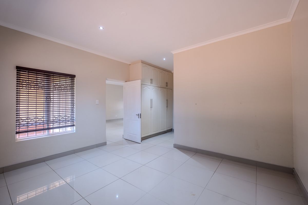 A bright, empty bedroom featuring neutral tiled flooring, built-in cupboards, and venetian blinds, offering a clean and versatile space.
