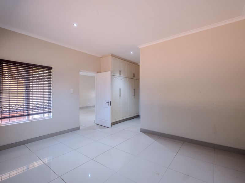 A bright, empty bedroom featuring neutral tiled flooring, built-in cupboards, and venetian blinds, offering a clean and versatile space.