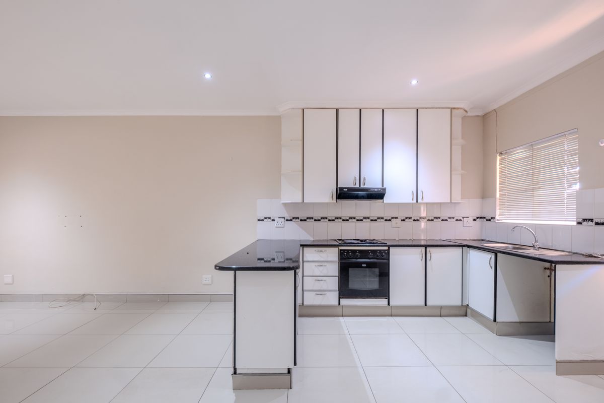 A clean, functional kitchen featuring white cabinetry, black granite countertops, built-in oven, hob, extractor fan, and tiled flooring in an open-plan layout.