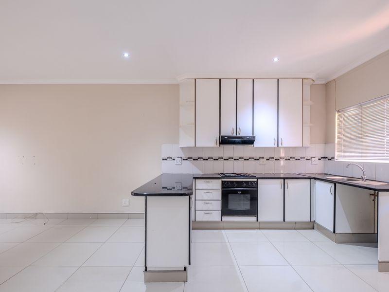 A clean, functional kitchen featuring white cabinetry, black granite countertops, built-in oven, hob, extractor fan, and tiled flooring in an open-plan layout.