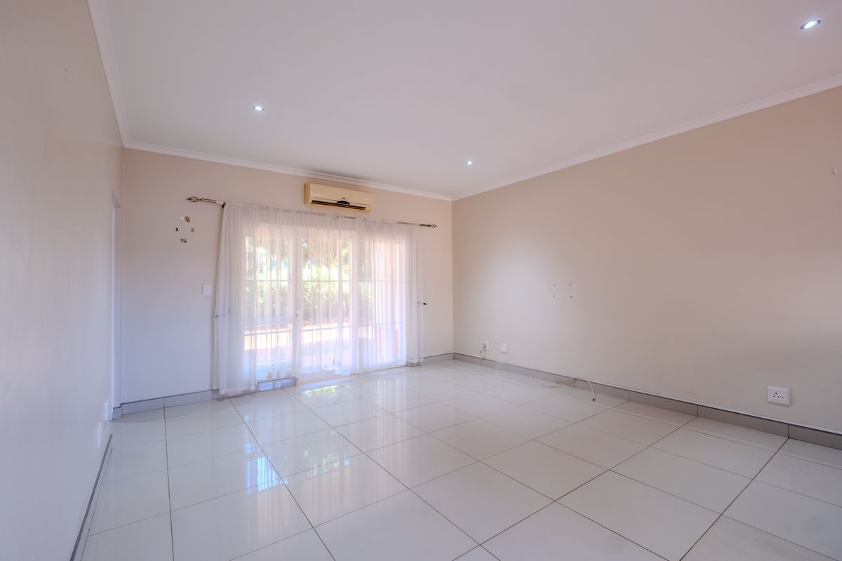 A bright, empty living room featuring polished tiled flooring, recessed downlights, and a wall-mounted air conditioning unit with access to an outdoor area.