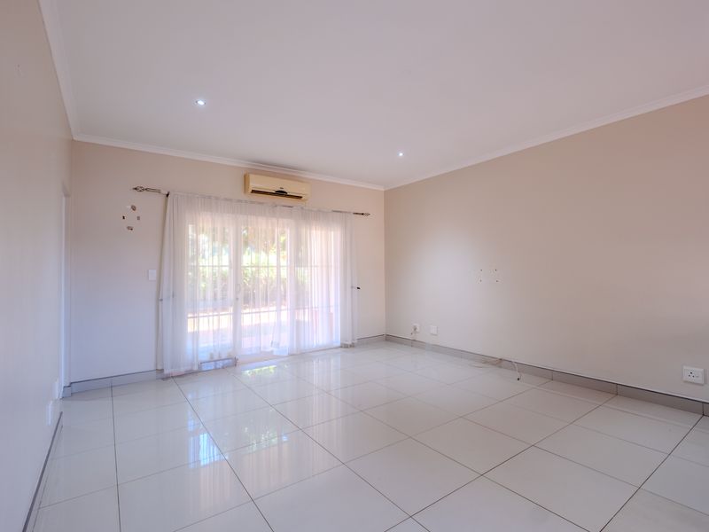 A bright, empty living room featuring polished tiled flooring, recessed downlights, and a wall-mounted air conditioning unit with access to an outdoor area.